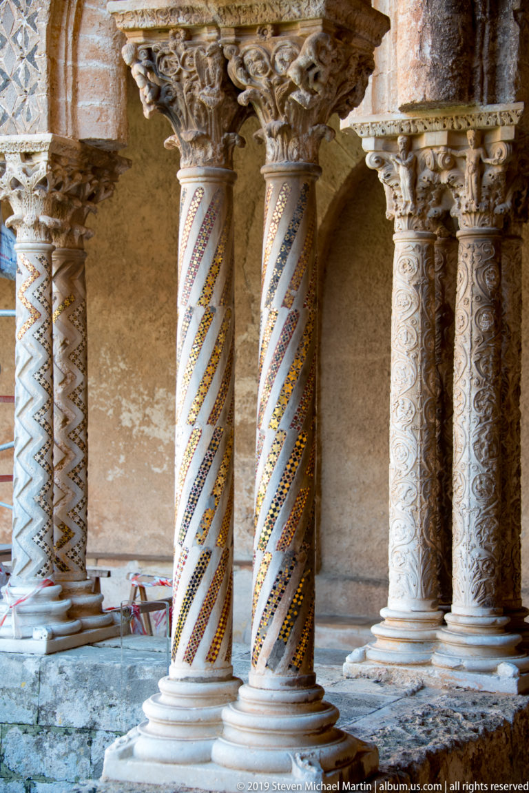 Carved capitals and geometric inlay decorate two columns beneath a cloister arch.