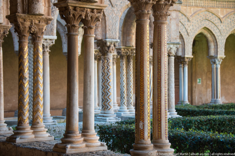 Ornamented cloister columns with patterned shafts, carved capitals, and garden arches behind.