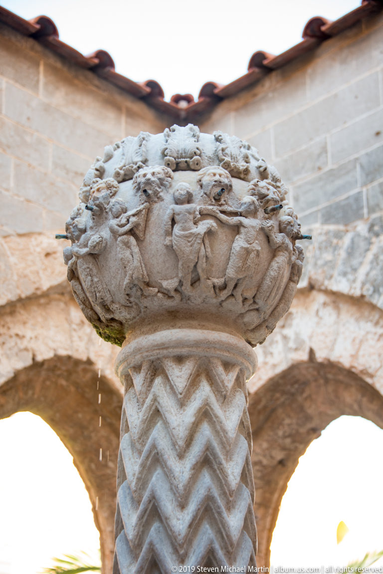 An upward view of the cloister fountain’s carved stone bowl and zigzag-patterned support.