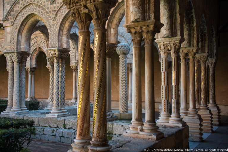 A shaded cloister arcade frames patterned columns and a fountain in the garden court.