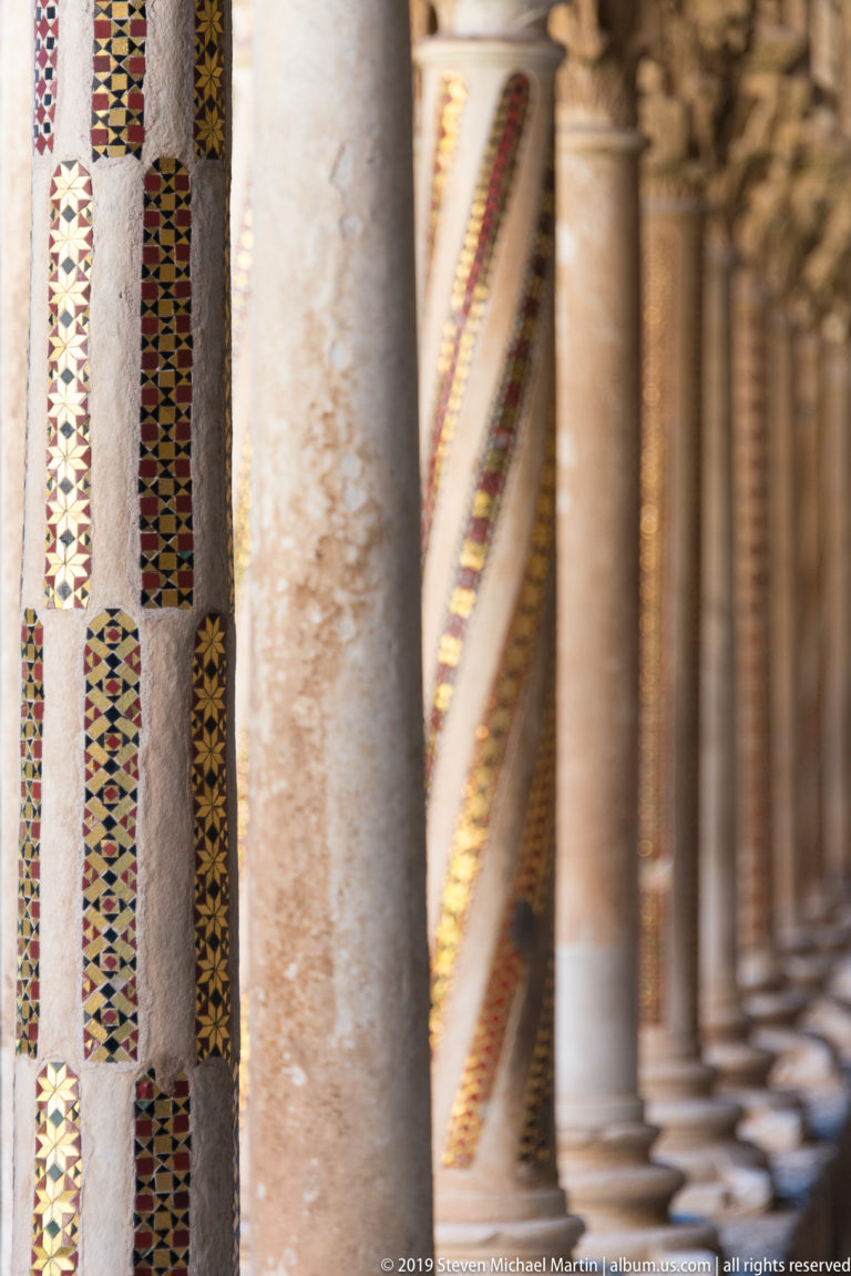 Adjacent cloister columns display alternating bands of colored geometric ornament.