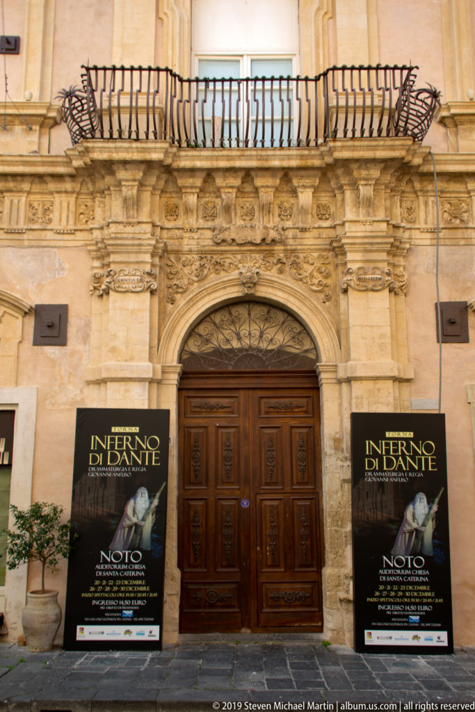 Carved limestone portal with a wooden double door and matching “Inferno di Dante” posters on both sides.