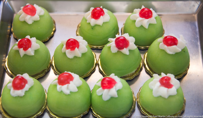 Green dome-shaped pastries on gold bases topped with white cream rosettes and red garnish.