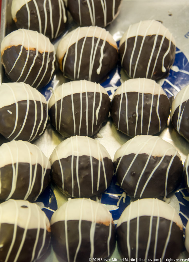 Rows of oval dark-chocolate-coated pastries decorated with thin white icing stripes on a display tray.