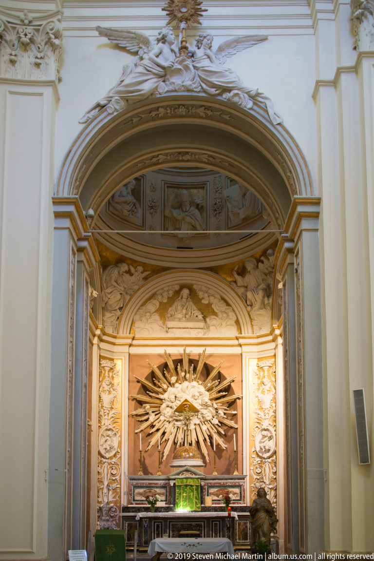 Ornate white-and-gold side chapel with a dove at the center of radiating golden rays above the altar.