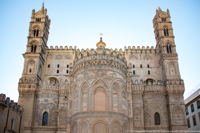 Frontal exterior view of Palermo Cathedral’s richly patterned rounded apse, flanked by tall towers and crenellated upper walls.