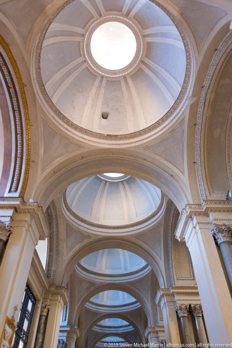 Upward axial view through repeated pale domed vaults with circular openings and arches receding into the cathedral.