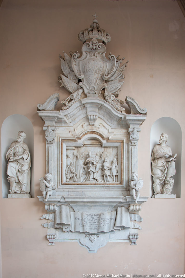 Elaborate pale wall memorial with central relief, crest, scrolling ornament, inscription panel, and busts in side niches.