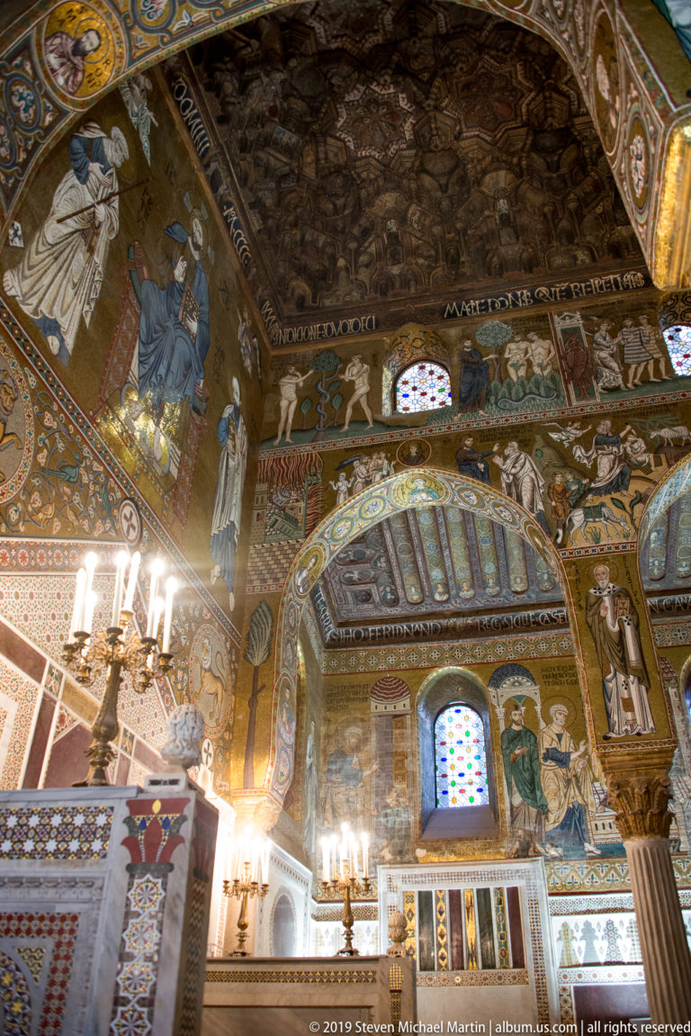 Oblique chapel interior with dark carved ceiling above gold mosaics, patterned arches, stained-glass windows, and marble wall panels.