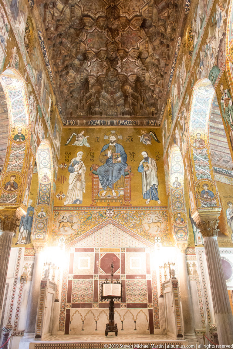 Gold mosaic of enthroned Christ between Saints Peter and Paul beneath the dark carved wooden ceiling of the Palatine Chapel.