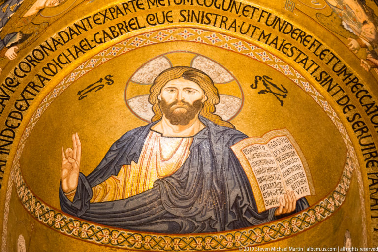 Close gold mosaic of Christ Pantocrator blessing with his right hand and holding an open Gospel book.