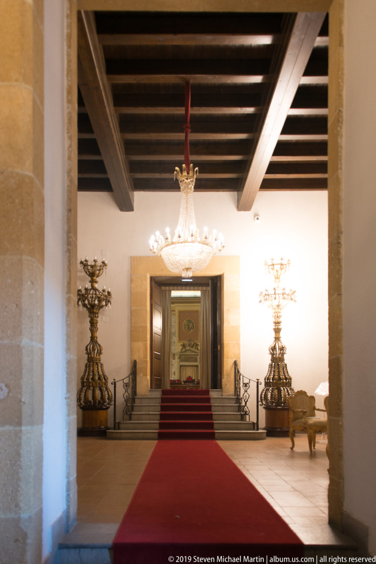 Red-carpeted ceremonial passage with chandeliers and candelabra.