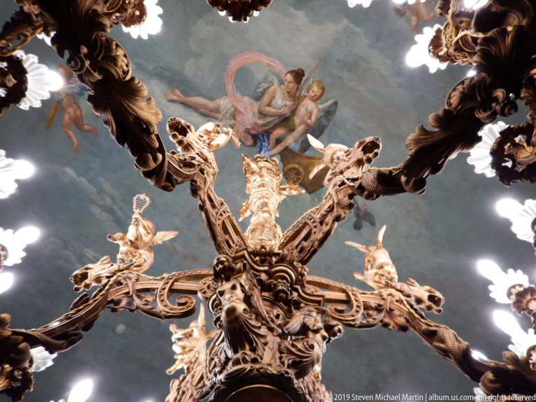 Sculptural chandelier viewed from below against a painted ceiling.