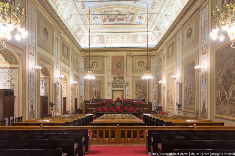 Ornate institutional assembly chamber with benches and raised dais.