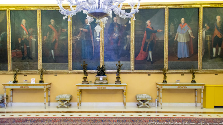 Historical court portraits above gilded console tables.