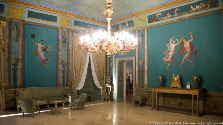 Blue state room with crystal chandelier and mythological wall panels.