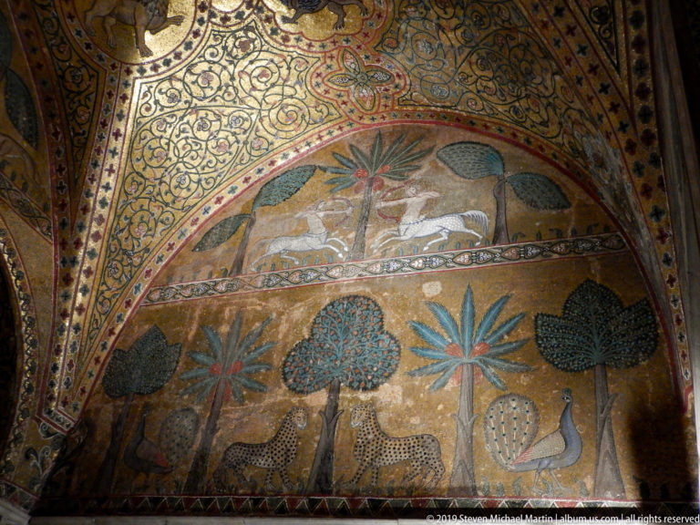 Arched gold mosaic showing stylized trees, facing peacocks, spotted quadrupeds, and birds beneath dense ornamental borders.