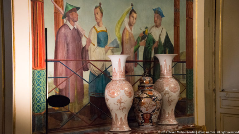 Three ornamental porcelain vases before a painted wall panel.