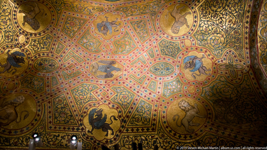 Vault covered with dense gold, red, green, and blue mosaic patterns and circular medallions containing animals.