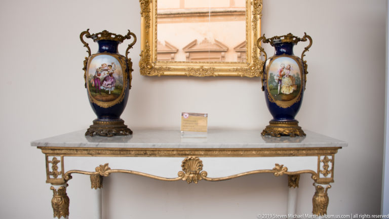 Two dark-blue porcelain vases with painted panels flank a gilded mirror above an ornate console table.