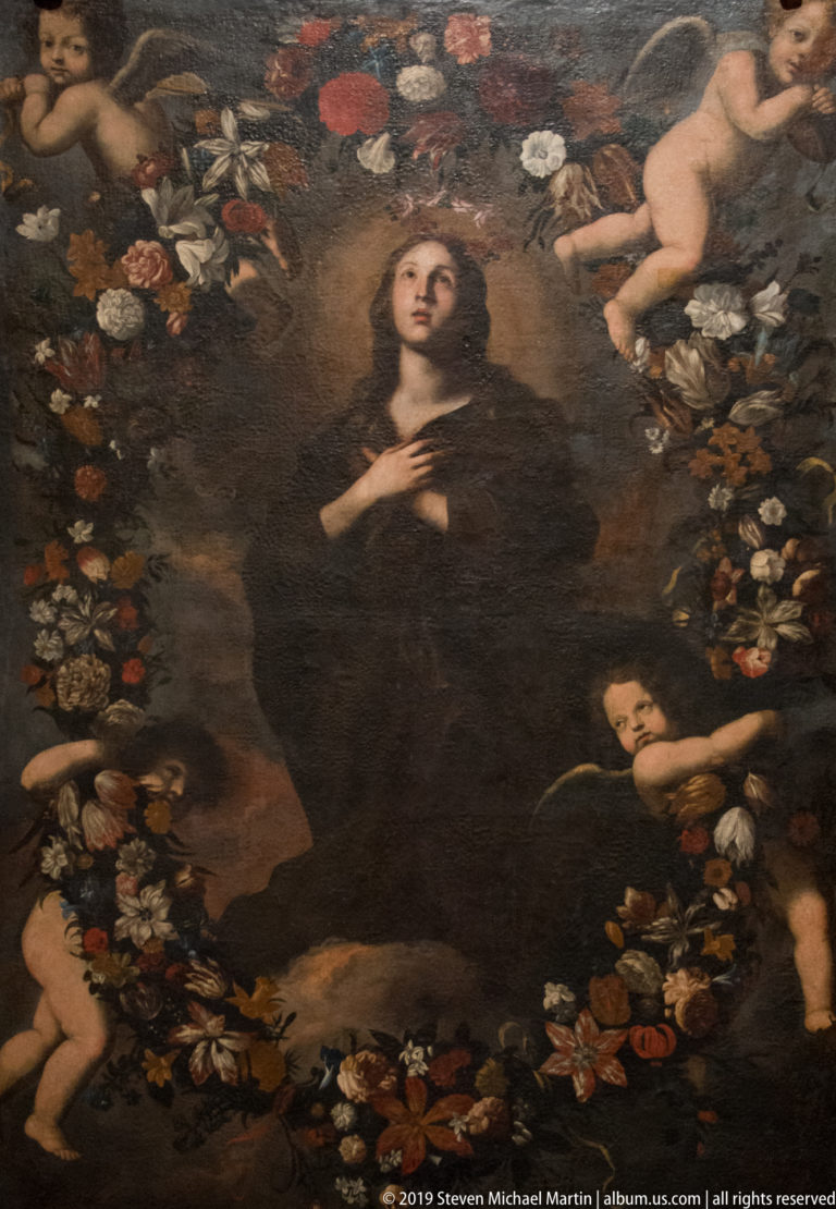 Dark-robed female saint stands amid abundant flowers, surrounded by small winged putti on a dark background.