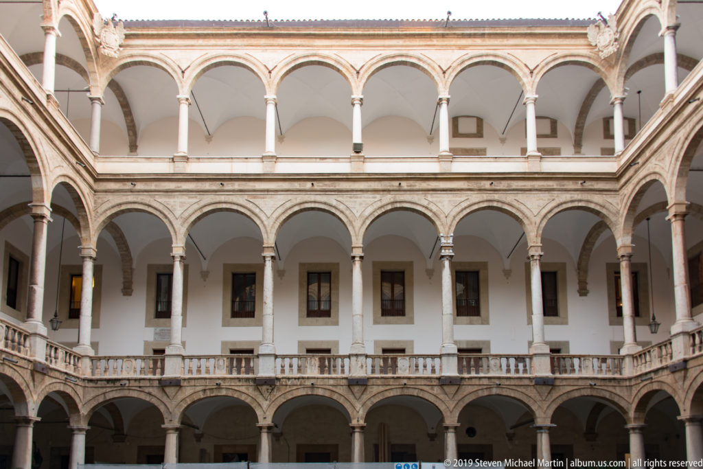 Two-story arcaded courtyard with repeated rounded arches, slender columns, and a balustraded upper gallery.