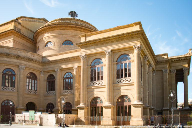 Sunlit side elevation of the Teatro Massimo with arched windows, projecting bays, and rounded upper volume.