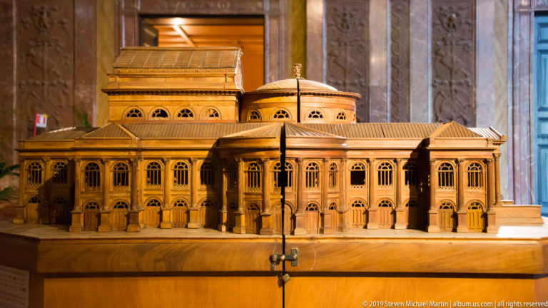Wooden architectural model of the Teatro Massimo showing arcaded wings, central roof volumes, and projecting portico.