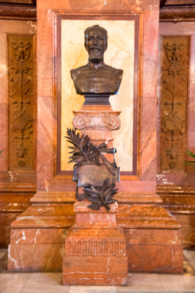 Dark bronze portrait bust on an ornate reddish stone and bronze pedestal inside the theater.