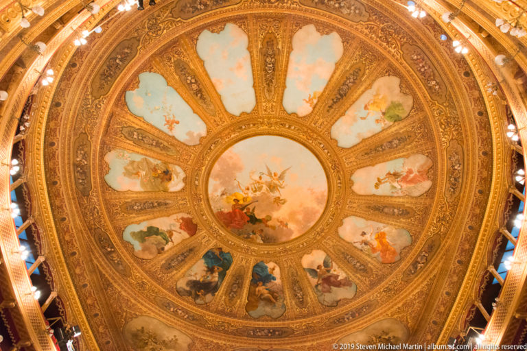 Complete circular theater ceiling with central sky scene, radial painted panels, gilding, and perimeter lights.