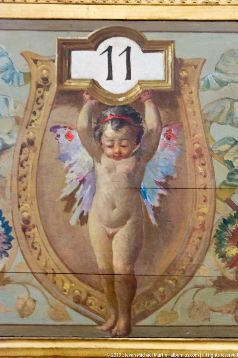 Close view of a painted winged cherub beneath the number 11, framed by flowers and ornament.