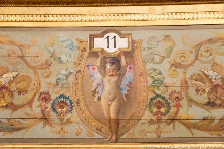 Painted cherub beneath the number 11 within a floral cartouche bordered by gilded molding.