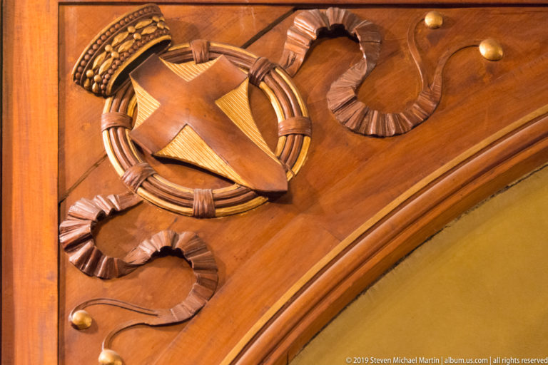Close-up of a carved wooden lyre inside a circular wreath with ribbon-like ornament and round bosses.