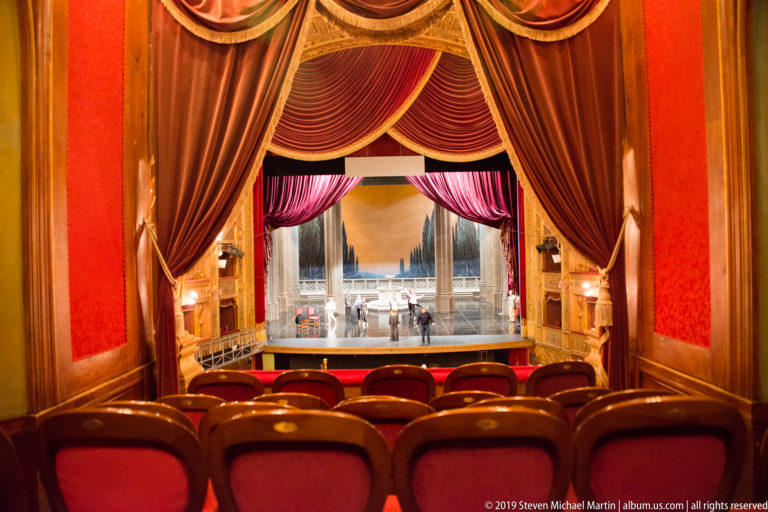 Red seats and heavy crimson draperies frame the stage as seen from inside a private theater box.