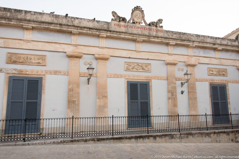 Classical façade of the Circolo di Conversazione with fluted pilasters, gray shutters, carved friezes, iron balcony, and rooftop inscription.
