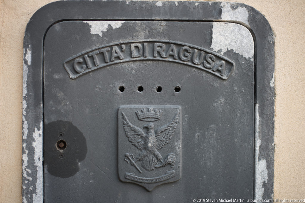 Gray cast-metal cover embossed “Città di Ragusa” with a crowned eagle civic emblem.