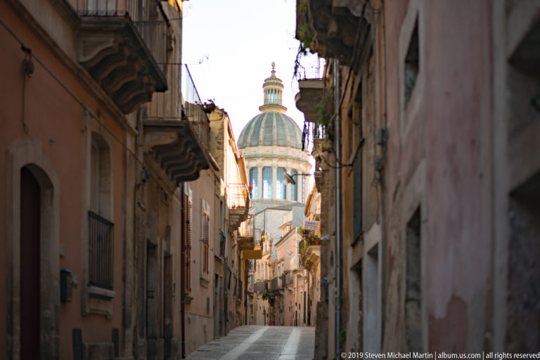 Narrow uphill street in Ragusa Ibla leading visually toward the illuminated dome of San Giorgio.