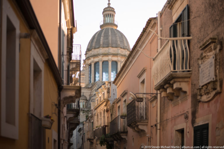 Ribbed dome of the Cathedral of San Giorgio framed by a narrow street of balconies and warm-toned façades.