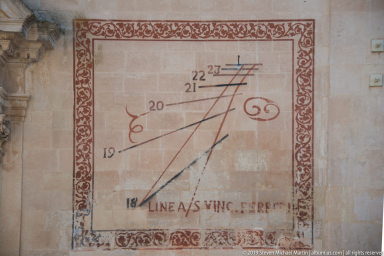 Painted wall sundial with red ornamental border, hour lines, numbers 18–23, and “Linea S Vinc. Ferreri” inscription.