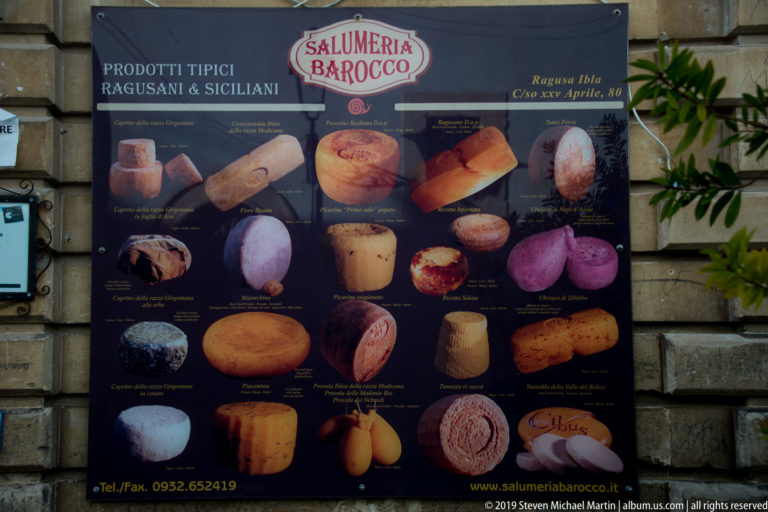 Salumeria Barocco sign displaying photographs and names of cured meats, cheeses, and other regional foods.