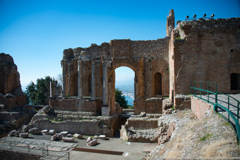 Large brick arch beside standing columns above excavated foundations and scattered stone blocks in the ancient theatre.