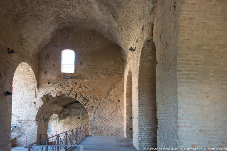 Ancient brick-vaulted interior with massive piers, arched openings, small windows, and a modern metal visitor walkway.