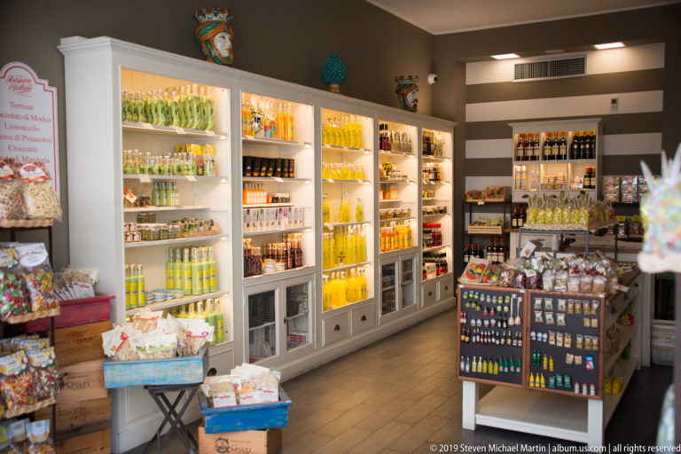 Bright specialty shop with illuminated shelves of colorful bottled liqueurs, packaged foods, sweets, and gift items.