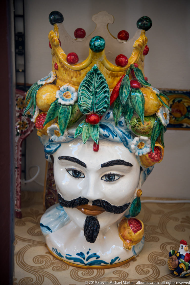 Glazed ceramic male head with moustache and beard, crowned by colorful modeled fruit, leaves, and decorative jewels.