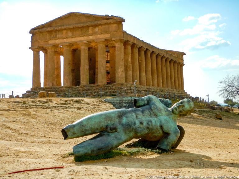 Large reclining green-patinated bronze figure in front of the intact golden Doric Temple of Concordia.