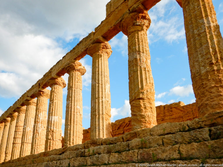 Low-angle oblique view of tall fluted Doric columns supporting surviving entablature blocks above stone steps.