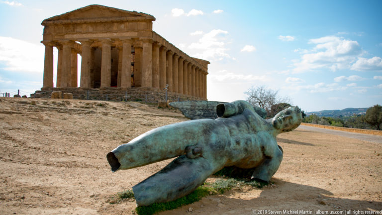 Large reclining green-patinated bronze figure in the foreground with the Temple of Concordia behind.