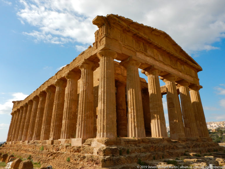 Three-quarter side view of the Temple of Concordia showing its long intact Doric colonnade, façade, and stepped base.