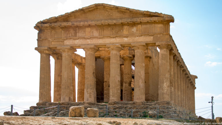 Warmly lit Temple of Concordia with pediment, Doric façade columns, side colonnade, rough foundations, and protective ropes.