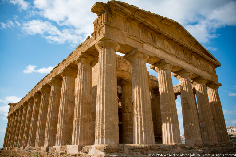 Low-angle corner view of tall fluted Doric columns supporting the Temple of Concordia's entablature and roofline.